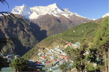 Namche Bazaar, full of buildings with colorful roofs, in the foreground of another mountain with snow at its peak.