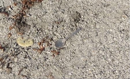 A steel spoon on a sandy ground.