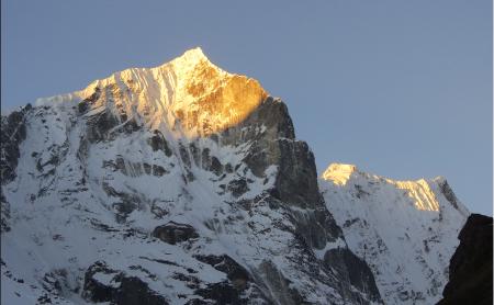 Sunlight falls on a peak, creating an orange glow on the snowy mountain.