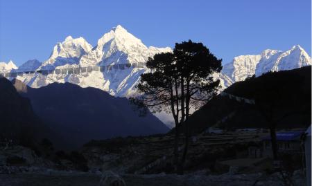 Prayer flags stand dimly illuminated in front of multiple snowcapped peaks.