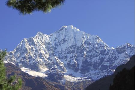 The peak of a snowclad Himalaya, with patches of melted snow revealing a black mountainface.
