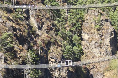 The two bridges in the foreground of a jagged cliffside. People are walking on the upper one, while the lower has a deserted enclosure in the middle of it.
