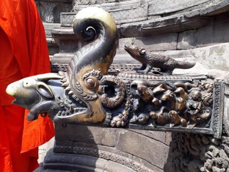 A side view of an intricate tap in Kathmandu, Nepal. The tap is made of metal, and it's decorated with a 3D sculpture of a crocodile eating a fish. The water comes out through the fish's mouth