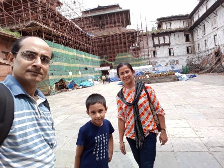A child and their parents, in the foreground of a big wood and mortar building under renovation at the Kathmandu Durbar Square, in Kathmandu, Nepal.